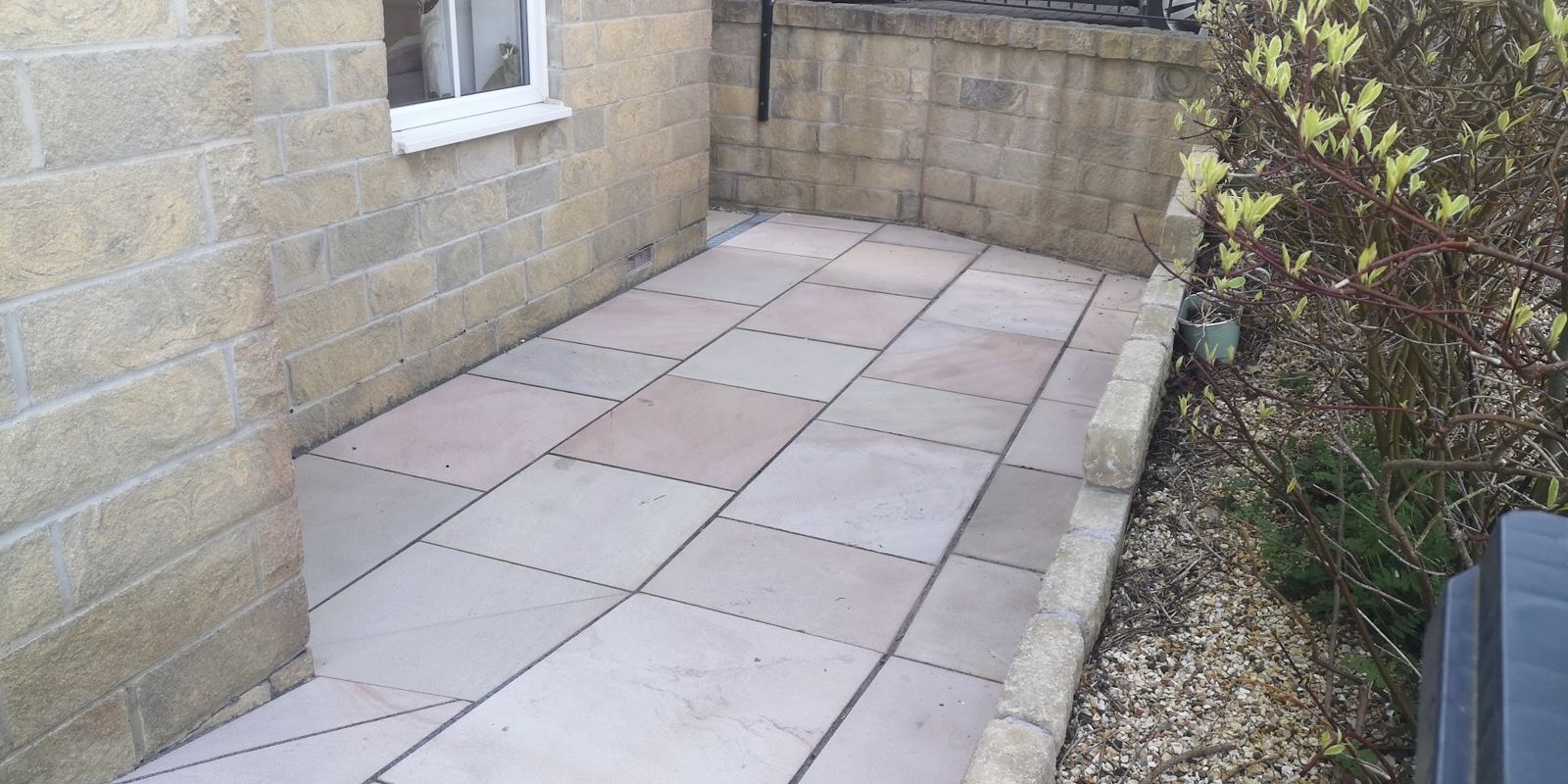 New stone path laid along the wall of a stone house, with a gravel border