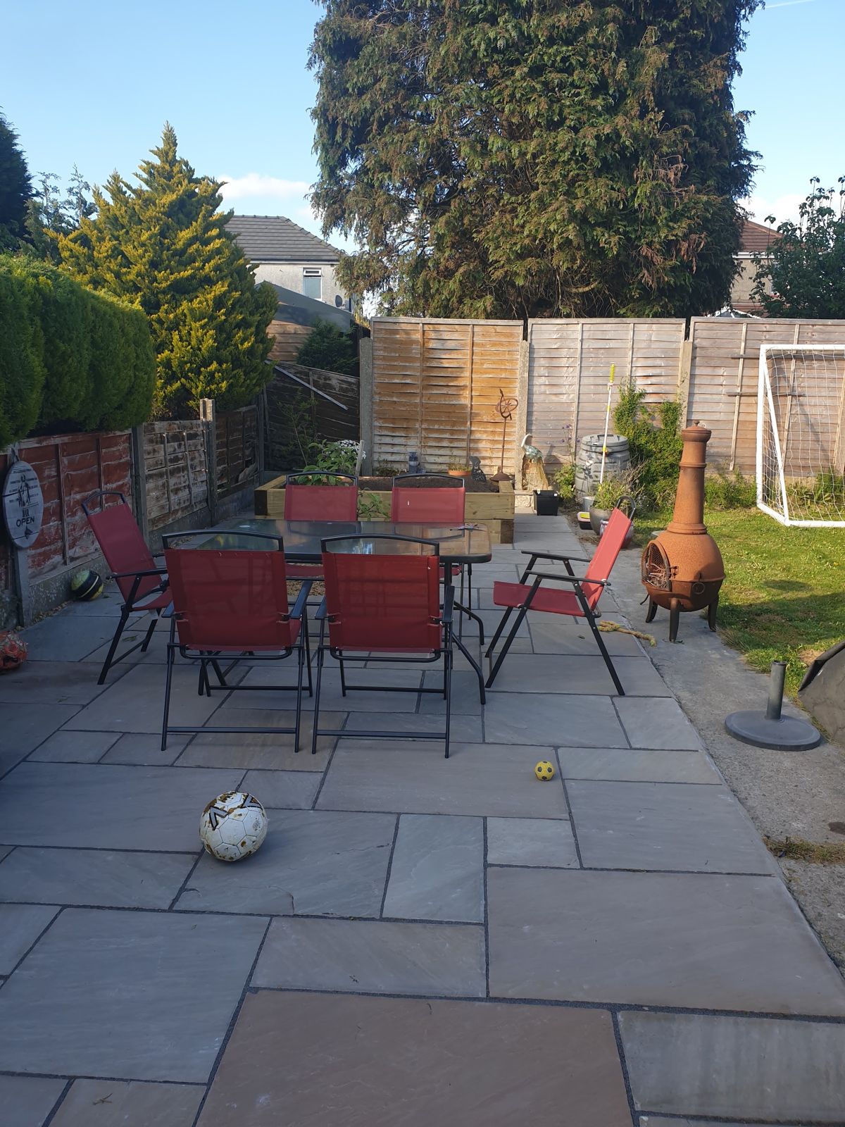 Large stone patio with garden table and chairs, lawn and fencing beyond