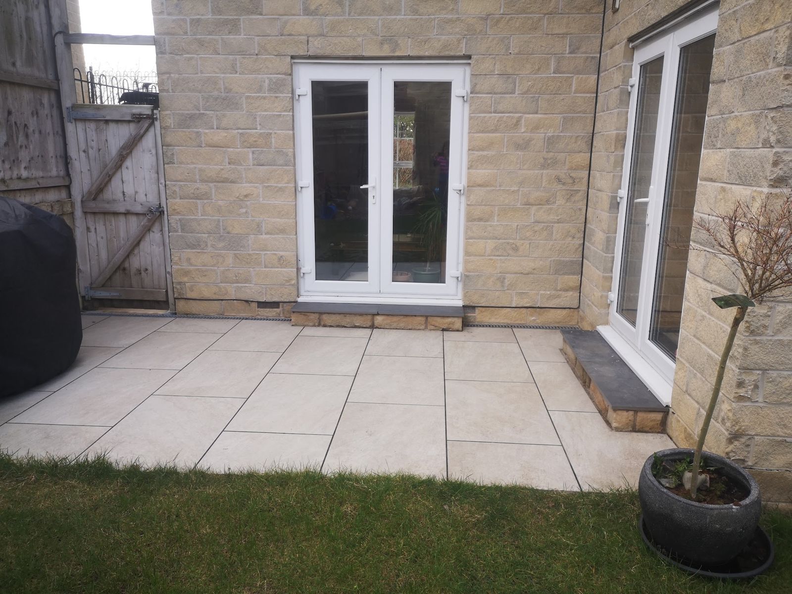 Pale stone patio laid outside patio doors, with a lawn edge